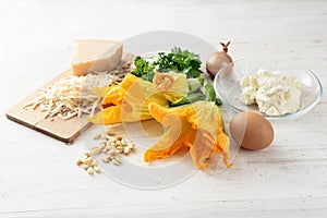 zucchini or courgette flowers and ingredients for a ricotta parmesan filling on a white wooden table, mediterranean appetizer rec