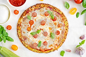 Zucchini crust pizza with tomato sauce, mozzarella cheese, fresh tomatoes and basil on a white wooden background.