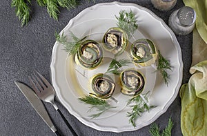 Zucchini and eggplant rolls with garlic and cream cheese on a plate on a dark gray background