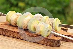 Zucchini and mushrooms on metal skewers on wooden chopping board