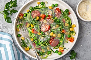Zucchini noodle with tomato, corn and green peas on white plate