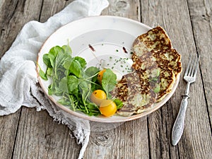 Zucchini pancakes with arugula and yellow cherry tomatoes on wood background. Copy space, close up.