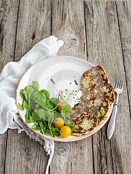 Zucchini pancakes with arugula and yellow cherry tomatoes on wood background. Copy space, close up.