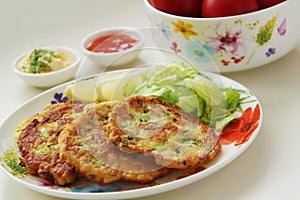 Zucchini pancakes. Vegetable fritters served with lemon and fresh salad. Yogurt and tomato sauces on background. Close up view.