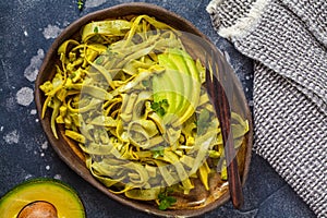 Zucchini pasta with pesto and avocado in dark dish. Healthy vegan food concept