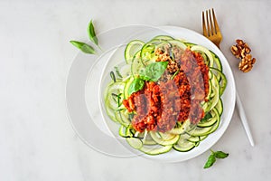 Healthy plant-based zucchini pasta topped with meatless walnut cauliflower bolognese, top view on a white marble background