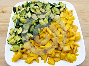 Zucchini and peppers in a white dish, wooden background.