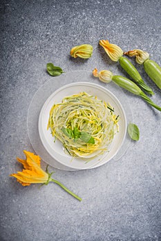 Zucchini vegetable noodles - green zoodles or courgette spaghetti on plate over gray background. Clean eating, raw vegetarian food