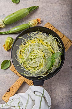 Zucchini vegetable noodles - green zoodles or courgette spaghetti on plate over gray background. Clean eating, raw vegetarian food