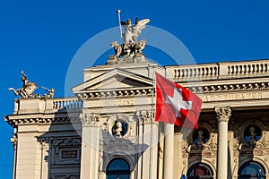Zurich Opera House and its rooftop sculptures with the flag of Switzerland against a clear blue sky