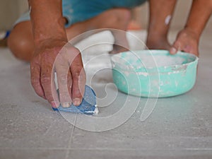 à¹‡Hand of a construction worker grunting ceramic tiles on the house floor - tiling work