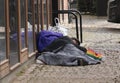 Homeless man lies sleeping on skt. Knuds Torv in Aarhus, It is a cold day and hand is on the hard stones