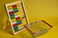 Abacus and shopping basket at yellow background. Shopping, personal finances, money spendings concept
