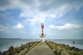 Abandon beacon light tower with concrete break water surrounded by sea water at sunny day.