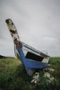 Abandon blue fiber boat stranded on the shore with soft and dramatic clouds