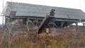 An abandoned board shed with a slate roof stands amidst a thicket of dry grass and bushes. A belt conveyor with an electric motor Royalty Free Stock Photo