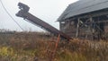 An abandoned board shed with a slate roof stands amidst a thicket of dry grass and bushes. A belt conveyor with an electric motor Royalty Free Stock Photo