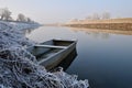 Abandoned old row boat moored by the river bank in winter. Calm river, frost