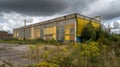 Abandoned Building Site Boarded factory with no windows, open ground space, uncut weeds growing, cloudy dark sky, nobody Royalty Free Stock Photo