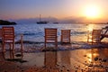 Abandoned chairs on a sandy beach after summer vacation while two boats cruise along before a golden sunset Royalty Free Stock Photo