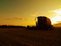 Abandoned combine harvest wheat in the middle of a farm field. Morning yellow wheat field on the sunset cloudy orange sky