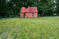 Abandoned damaged brick shed behind a green meadow