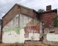 Abandoned derelict old house with crumbling brick walls propped up with scaffolding and overgrown with ivy