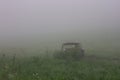 Abandoned destroyed car in a green field covered with fog - creates a creepy image Royalty Free Stock Photo