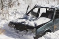 Abandoned destroyed car in the snow. Skeleton of unnecessary transport with broken headlights