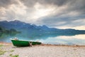 Abandoned fishing paddle boat on bank of Alps lake. Morning lake glowing by sunlight. Royalty Free Stock Photo