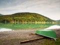 Abandoned fishing paddle boat on bank of Alps lake. Morning lake glowing by sunlight. Royalty Free Stock Photo