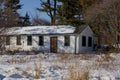 Abandoned house - windows blocked, electricity wires cut, snow covered field with trees in the background. Spring, sunny day.