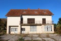 Abandoned large family house with closed wooden window blinds and long front balcony surrounded with concrete tiles and overgrown