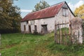 Abandoned old barn with wooden fence and grass on backyard. Weathered exterior of ancient building in village. Rural landmark.