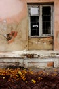 Abandoned old building exterior with peeling paint dirty wall window and fallen yellow leaves. Royalty Free Stock Photo