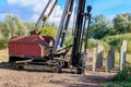 Abandoned old rusty pile driving machine on the glade against green trees and bushes in sunny day