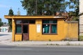 Abandoned old security guard building with cracked wooden doors and facade with trees and construction material in background