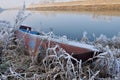 Abandoned old small boat on the river shore in winter.  Ice covered boat and plants. Royalty Free Stock Photo