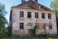 Abandoned old two-story apartment building with scuffed plaster, broken glass, partially collapsed roof tiles and boarded-up door