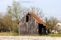 Abandoned old wooden barn with broken dilapidated wooden boards next to unused paved parking lot surrounded with uncut grass