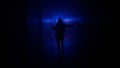 Portrait of female in hallway blue neon light. Close back shot woman walking cautiously in the dark corridor, holding up