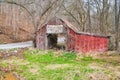 Abandoned red barn with faded paint and old sign by road in late winter Royalty Free Stock Photo