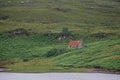 An abandoned red cottage on a hillside by a lake Royalty Free Stock Photo