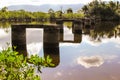 Abandoned ruins of a bridge over the river. Vegetation and clouds in the background.