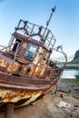 An abandoned rusty ship on a sandy beach and a backdrop of mount