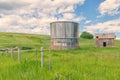 Abandoned Shed and Grain Silo Behind a Barbed Wire Fence in Summer