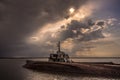 abandoned ship in the water with a dramatic sky with sun behind the clouds