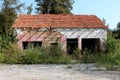 Abandoned small red brick family house with facade and roof tiles destroyed during war surrounded with overgrown grass and trees Royalty Free Stock Photo