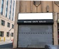 Abandoned Store Front Of Business That Went Bankrupt. The Security Gate Is Closed. Sign Says, Blow Out Sale.