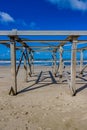 Abandoned structure with wooden posts and beams on the beach with the sea with small waves and foam in the background Royalty Free Stock Photo